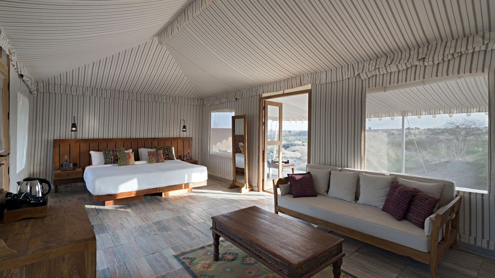 Interiors of a tent which is spacious and has double size bed, sofa, centre table, and a cabinet table with tea and coffee maker at MANVAR Kumat Thar Serenity Camp.