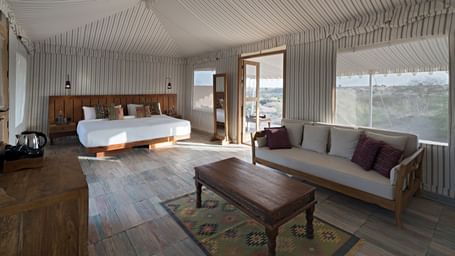 Interiors of a tent which is spacious and has double size bed, sofa, centre table, and a cabinet table with tea and coffee maker at MANVAR Kumat Thar Serenity Camp.