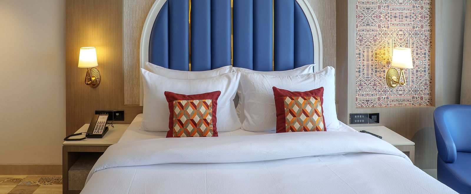 A hotel room showcases a bed with a blue arched headboard, bedside tables, and soft lighting - Melior Inn