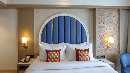 A hotel room showcases a bed with a blue arched headboard, bedside tables, and soft lighting - Melior Inn