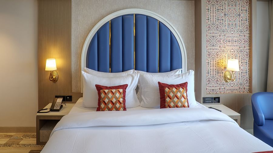 A hotel room showcases a bed with a blue arched headboard, bedside tables, and soft lighting - Melior Inn