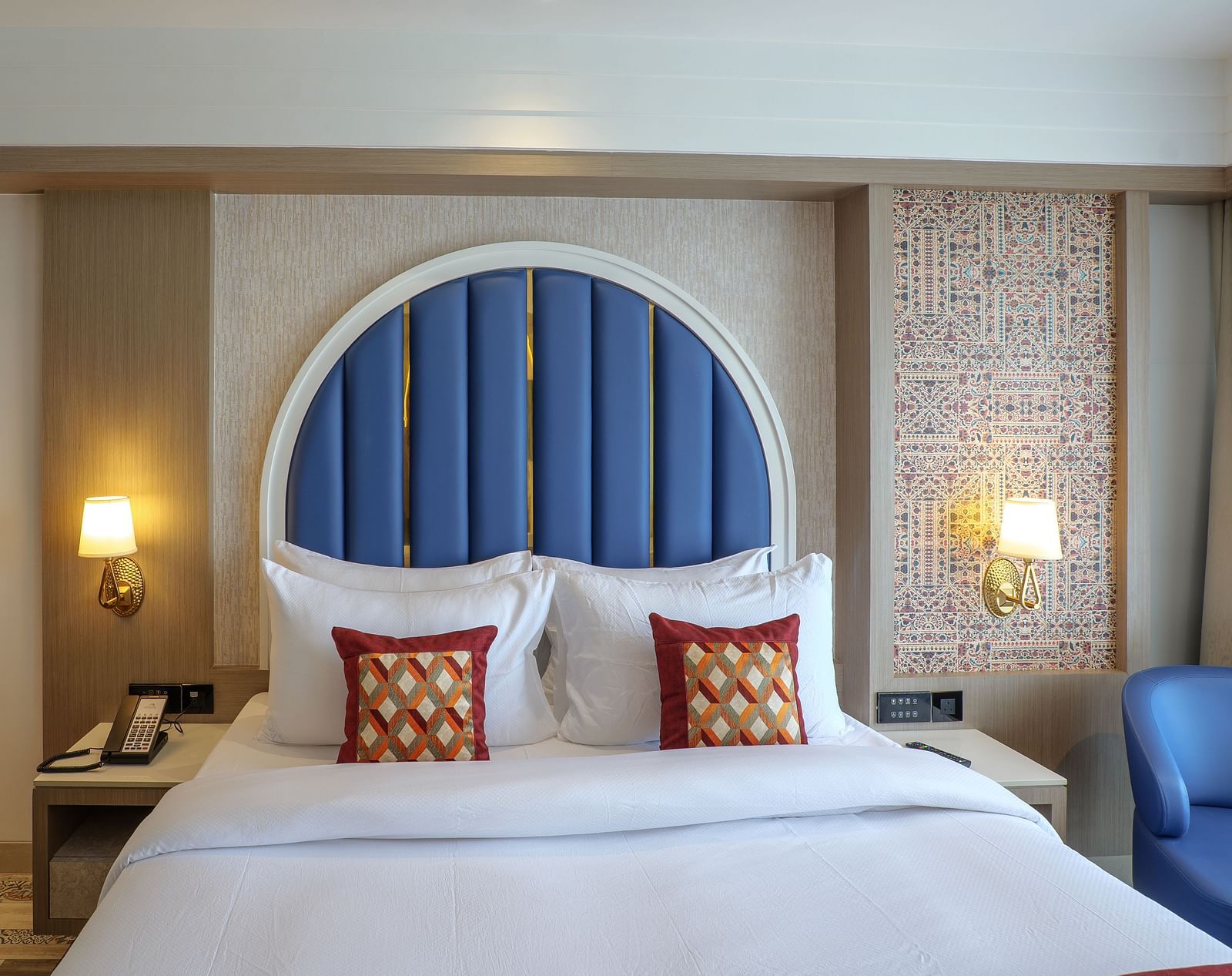 A hotel room showcases a bed with a blue arched headboard, bedside tables, and soft lighting - Melior Inn