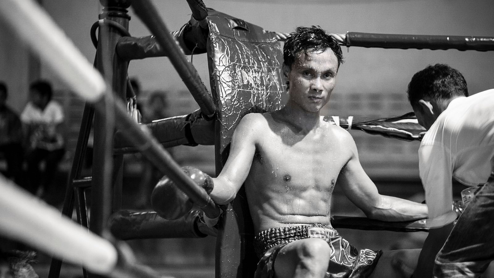 A muay thai fighter sitting in a corner after a round of fighting 