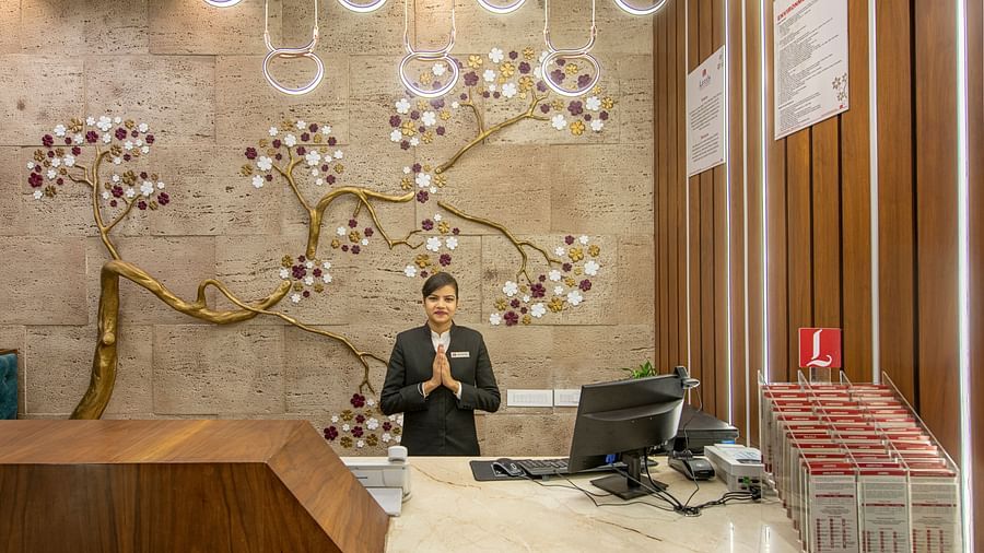 A hotel reception area with a patterned wall and a staff member - SK Lords Inn Ahmedabad