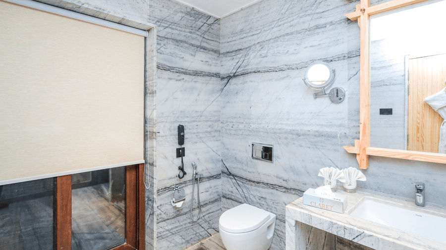 A washroom shows a basin with a mirror, a toilet, a shower space and a window with a blind at Ananta Spa & Resort, Jaipur.