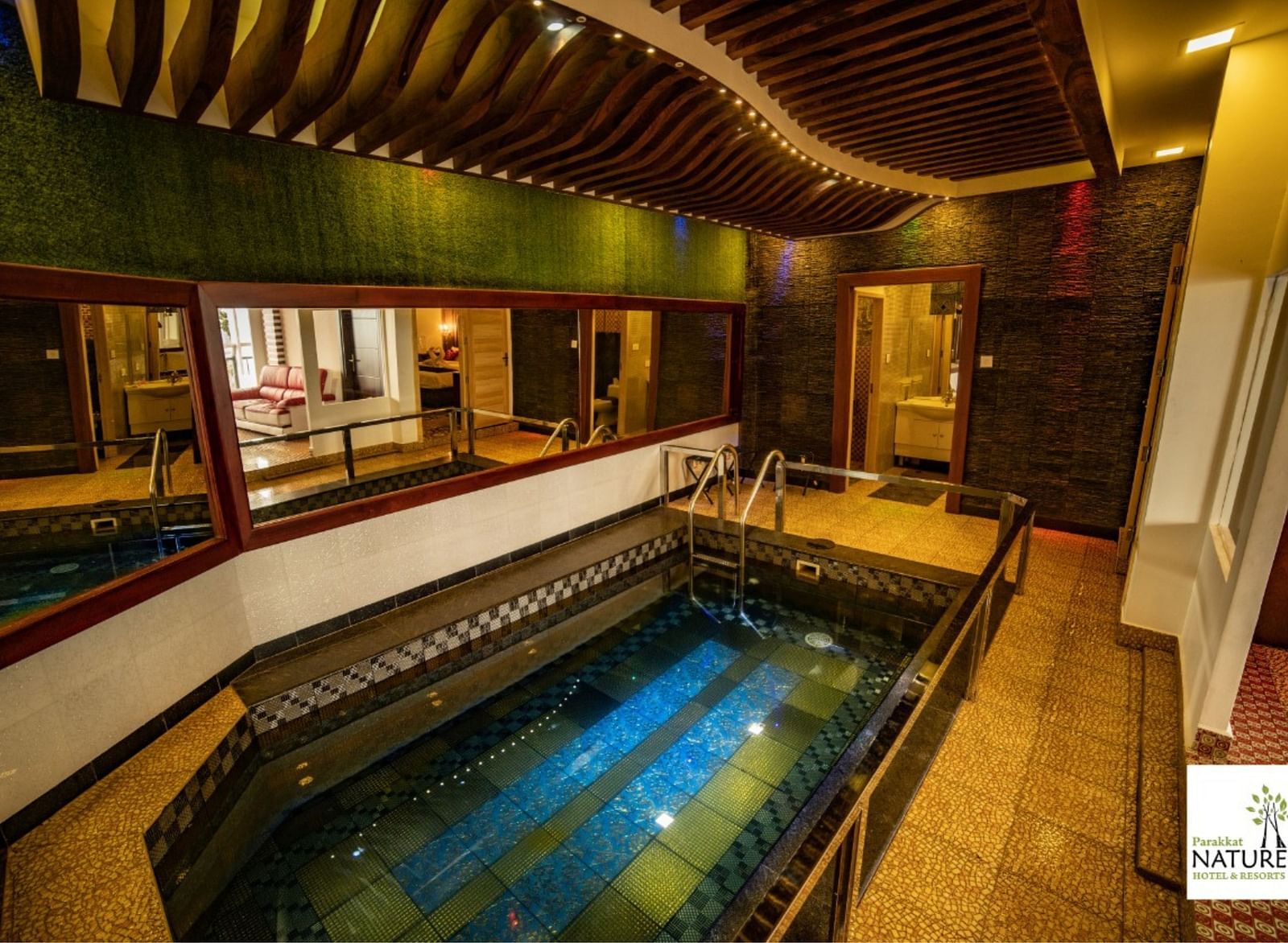 A small swimming pool inside Parakkat Nature Hotels and Resorts surrounded by mirrors on walls and rooms 