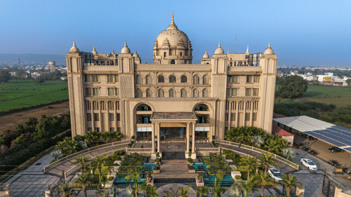 A grand palace-style facade of Classic Sapphire Ananta, Bundi with a large central dome flanked by smaller domes ornate a entrance driveway and landscaped gardens viewed from an elevated angle.