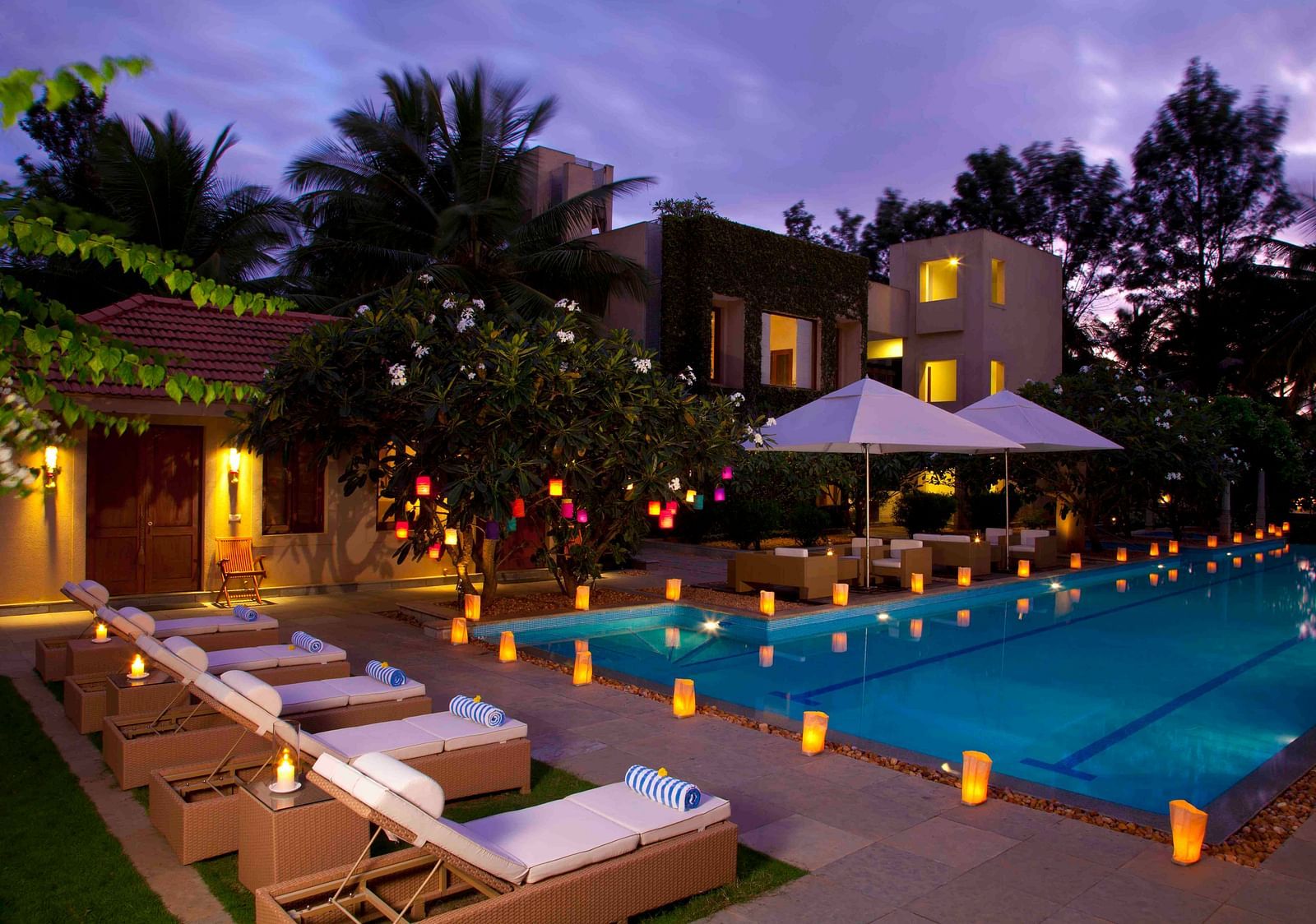 Outdoor evening view of a resort with a pool and lounge chairs, warm lighting - Shreyas Retreat