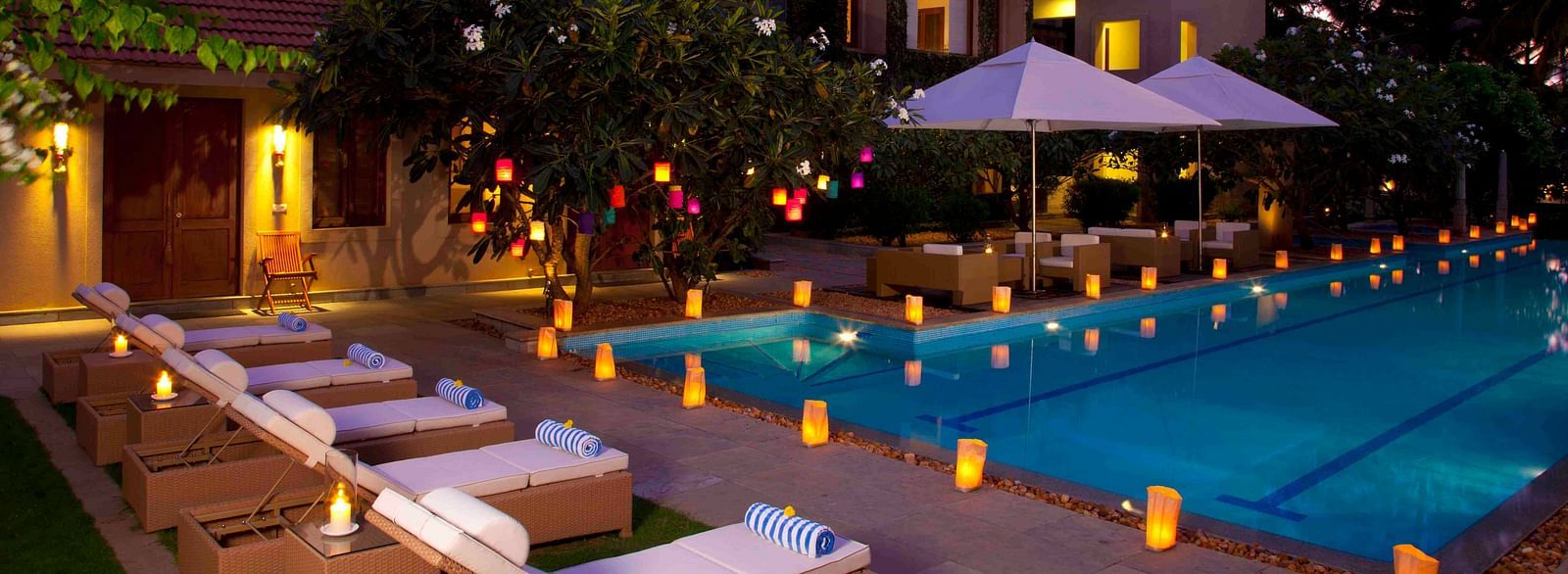 Outdoor evening view of a resort with a pool and lounge chairs, warm lighting - Shreyas Retreat