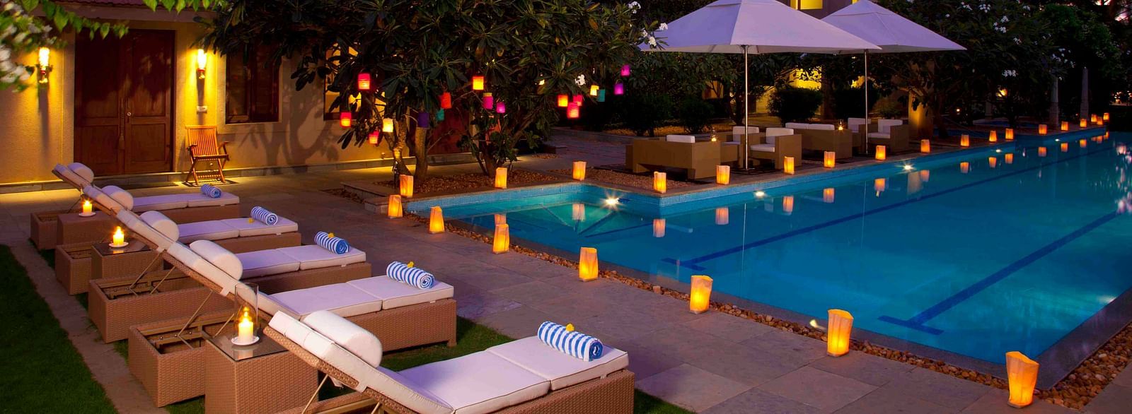 Outdoor evening view of a resort with a pool and lounge chairs, warm lighting - Shreyas Retreat