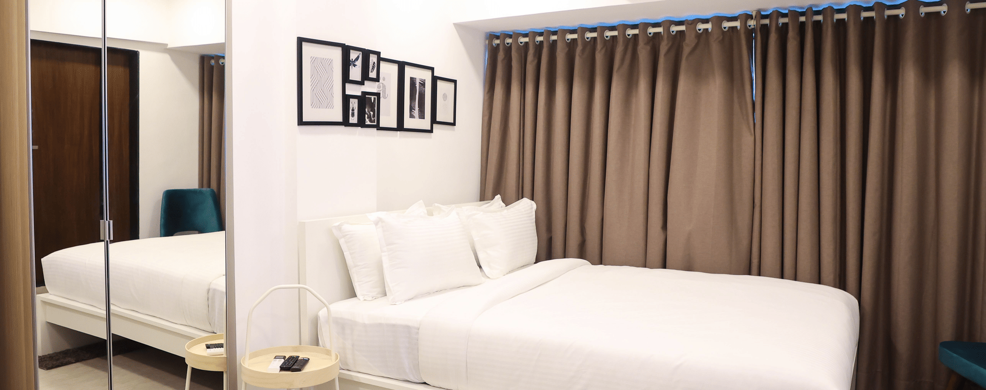 Bedroom at Wabi-Sabi, Juhu with a white double bed, taupe curtains, a mirrored wardrobe, and monochrome framed prints above the headboard.
