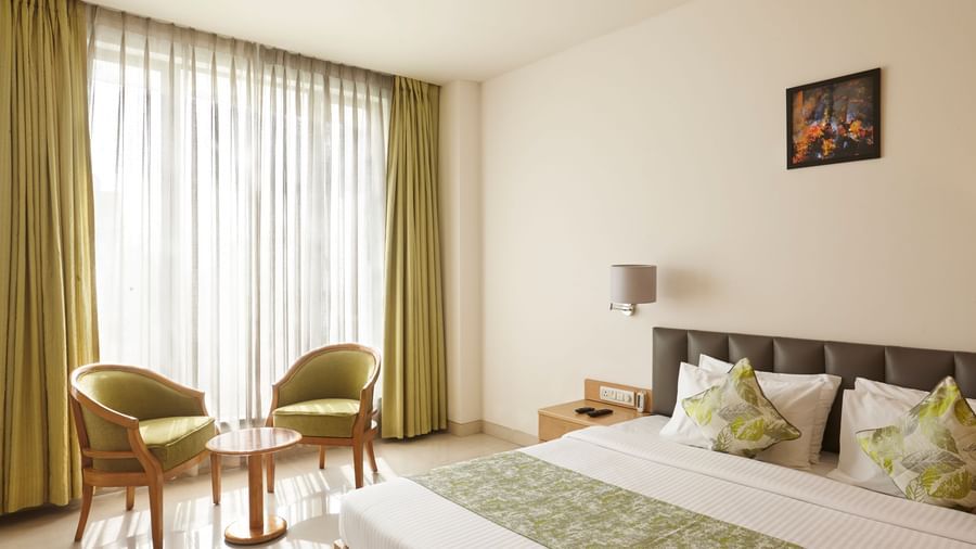 A bright hotel room at Monday Hotels Mahape, Navi Mumbai, with a bed, seating chairs by the window, and a TV.
