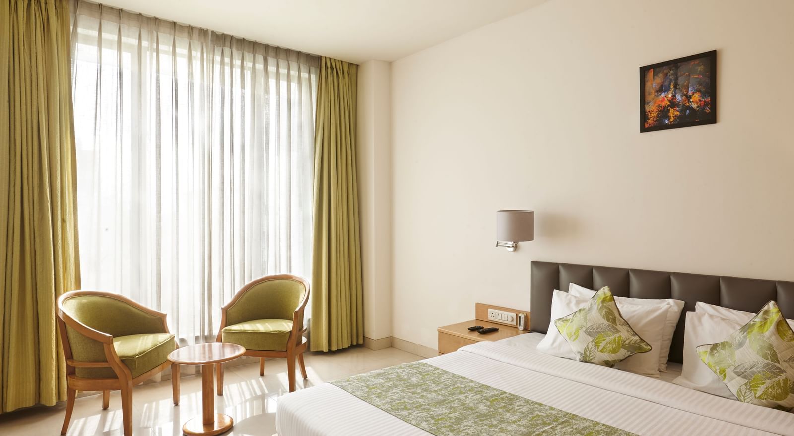 A bright hotel room at Monday Hotels Mahape, Navi Mumbai, with a bed, seating chairs by the window, and a TV.