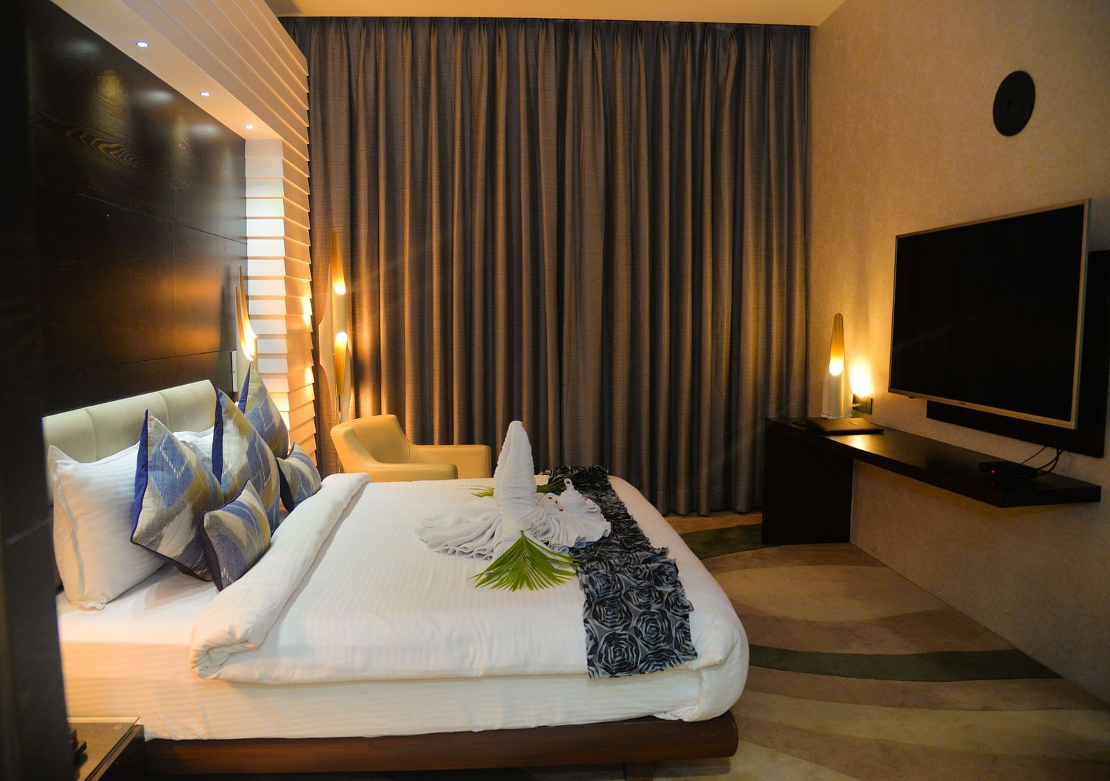 A room consisting of a neat bed a side drawer and a TV - Golden Blossom Imperial Resorts Lucknow