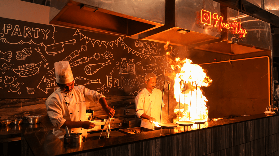 Chefs preparing food in live kitchen with open counter at Pravasa Hotel, Kolhapur.