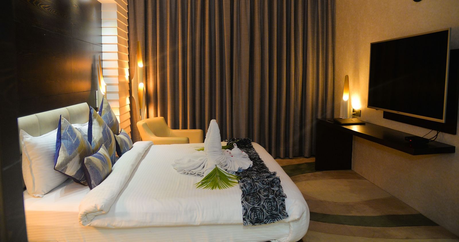 A room consisting of a neat bed a side drawer and a TV - Golden Blossom Imperial Resorts Lucknow
