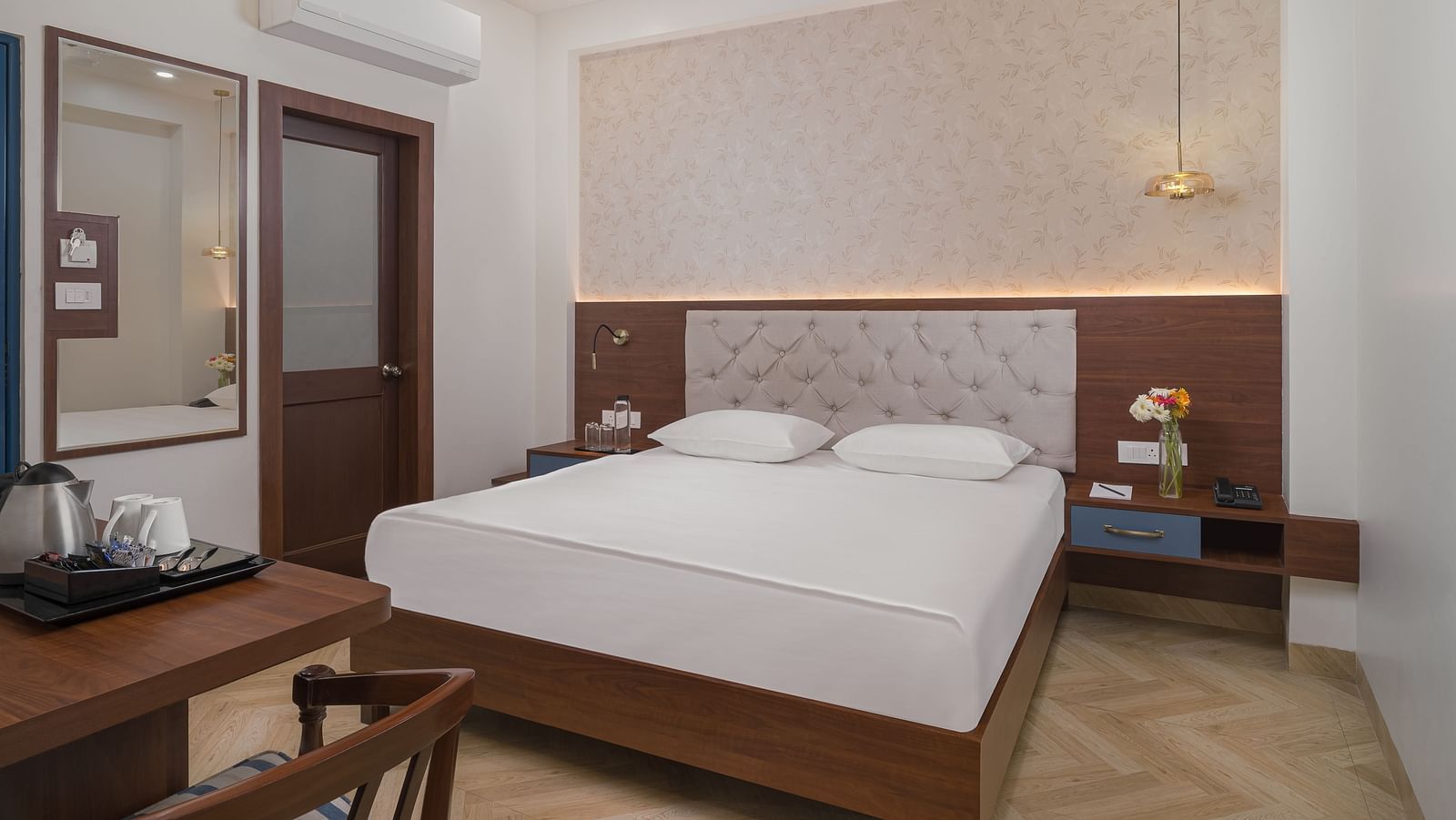 A spacious room features a large bed with a cushioned headboard, wooden bedside tables on either side, and inviting lighting | Hotel Ganga Maiya