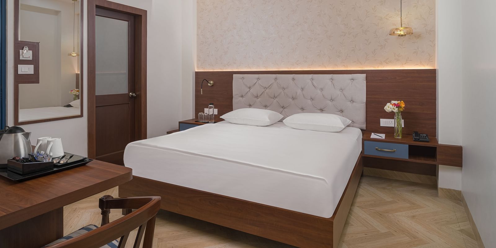 A spacious room features a large bed with a cushioned headboard, wooden bedside tables on either side, and inviting lighting | Hotel Ganga Maiya