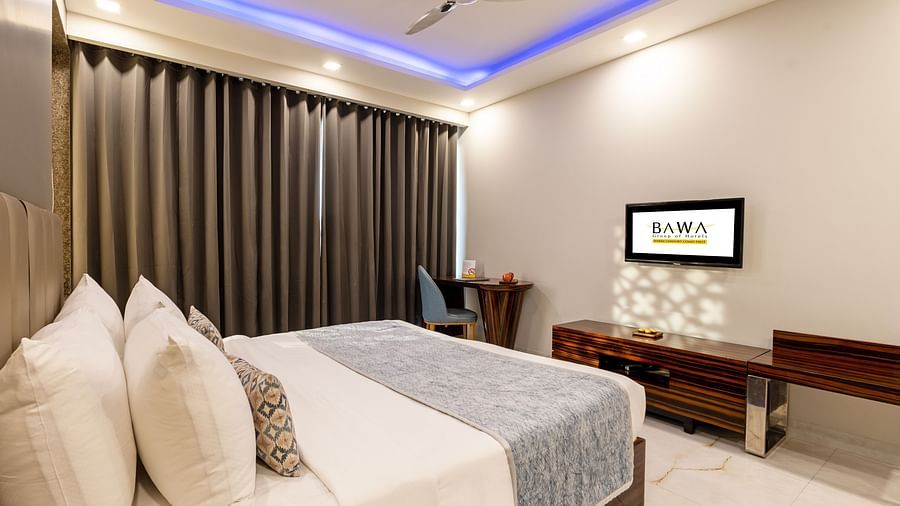Spacious room with a bed, wooden furniture, and stylish lighting at Hotel Bawa, Gurgaon.