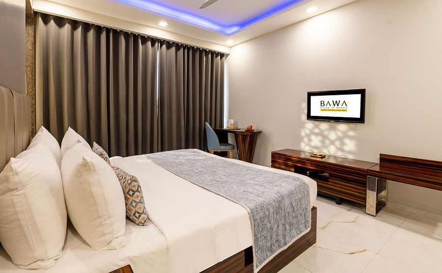 Spacious room with a bed, wooden furniture, and stylish lighting at Hotel Bawa, Gurgaon.