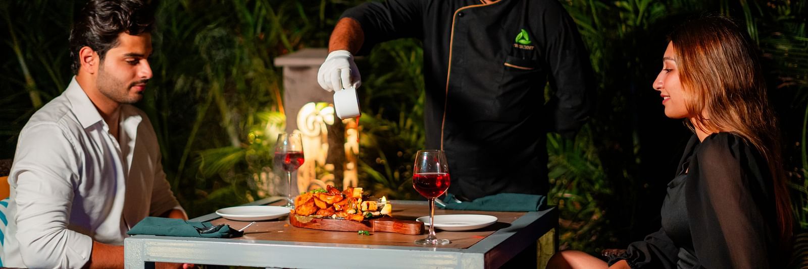 A chef serving a couple seated by the poolside, enjoying a delightful dining experience at Crescent Spa & Resort, Indore