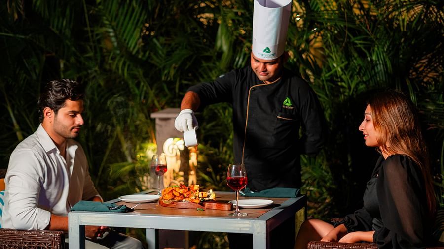 A chef serving a couple seated by the poolside, enjoying a delightful dining experience at Crescent Spa & Resort, Indore