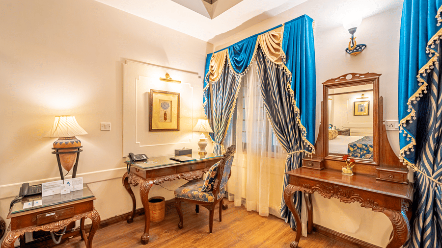 A classic study and dressing area within the Crown Club Suite at Noor-Us-Sabah Palace, decorated with heavy blue curtains and antique-style wooden furniture.