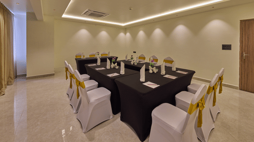 A beautifully lit banquet hall with a navy blue-draped long table surrounded by chairs wrapped in white covers