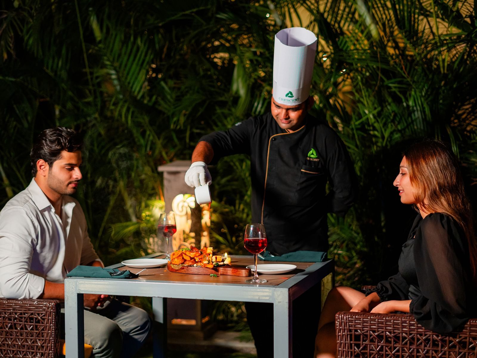 A chef serving a couple seated by the poolside, enjoying a delightful dining experience at Crescent Spa & Resort, Indore