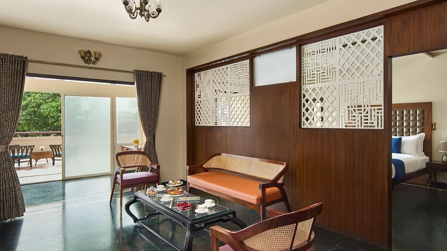 living room of Signature Suite with a mix of wooden and modern furniture, opening to a balcony with outdoor seating and a view of greenery at DGV Resort by Treat, Silvassa.