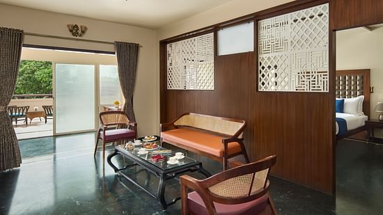 living room of Signature Suite with a mix of wooden and modern furniture, opening to a balcony with outdoor seating and a view of greenery at DGV Resort by Treat, Silvassa.