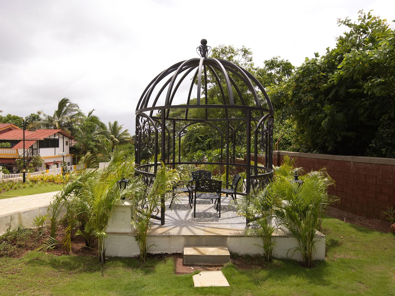 A pergola surrounded by lush greenery and plants along with a pathway going from the side of it at Imperial Goa.