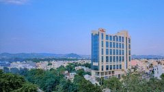 Pride Premier Udaipur Facade set amidst green trees and a backdrop of blue sky