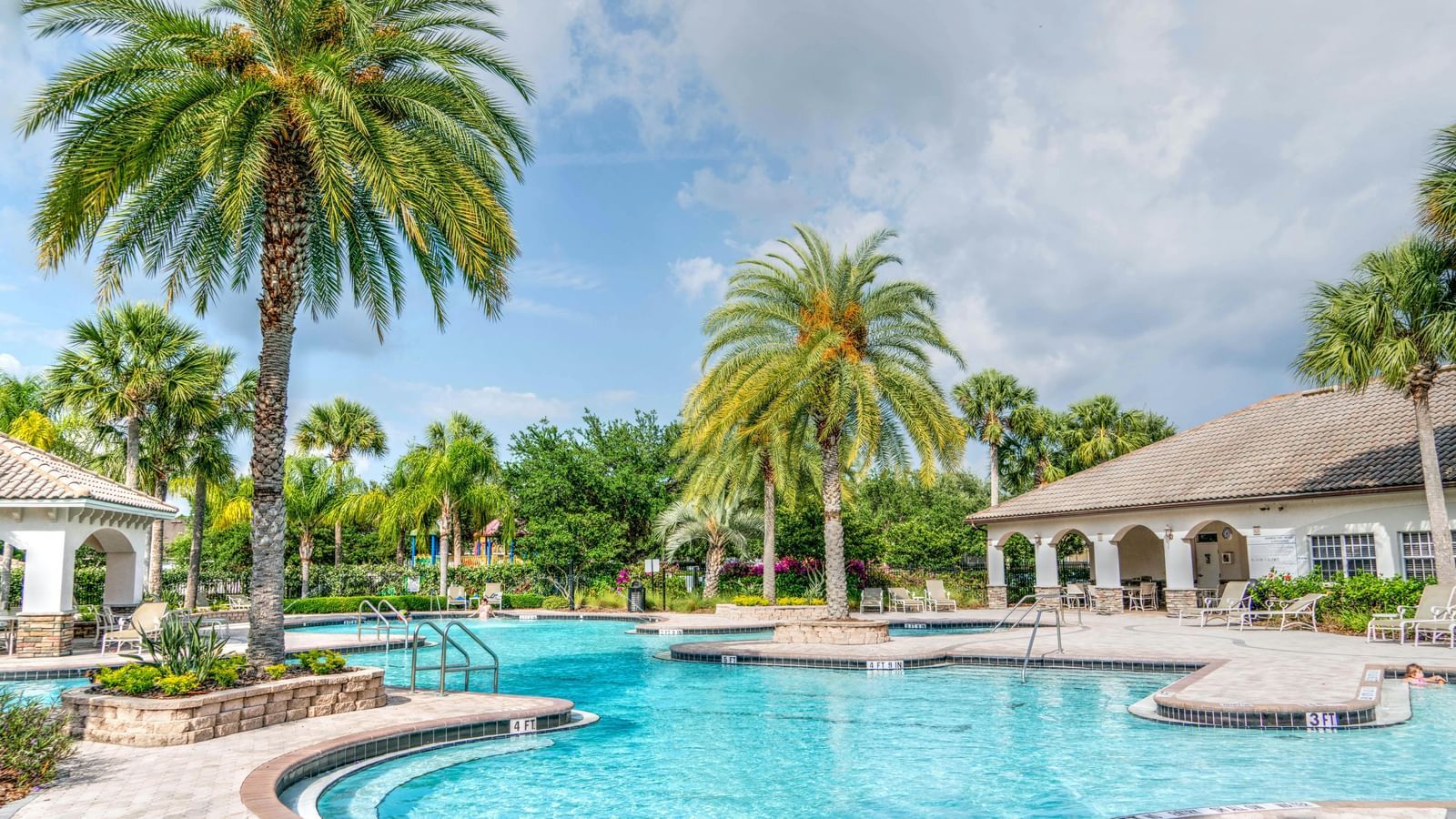A pool with palm trees and rooms surrounded with blue sky