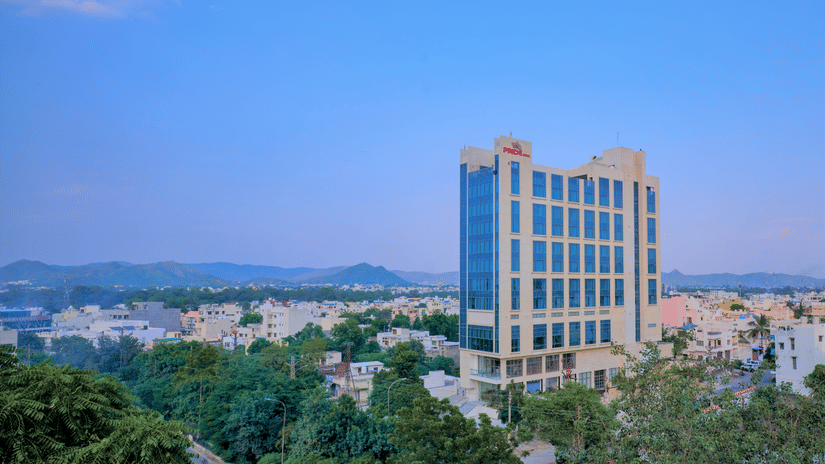 Pride Premier Udaipur Facade set amidst green trees and a backdrop of blue sky