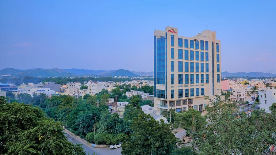 Pride Hotel Udaipur Facade set amidst green trees and a backdrop of blue sky