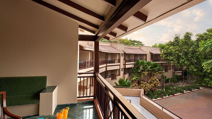 balcony of Executive Suite with a couch and a table, offering a view of other buildings and greenery at DGV Resort by Treat, Silvassa.