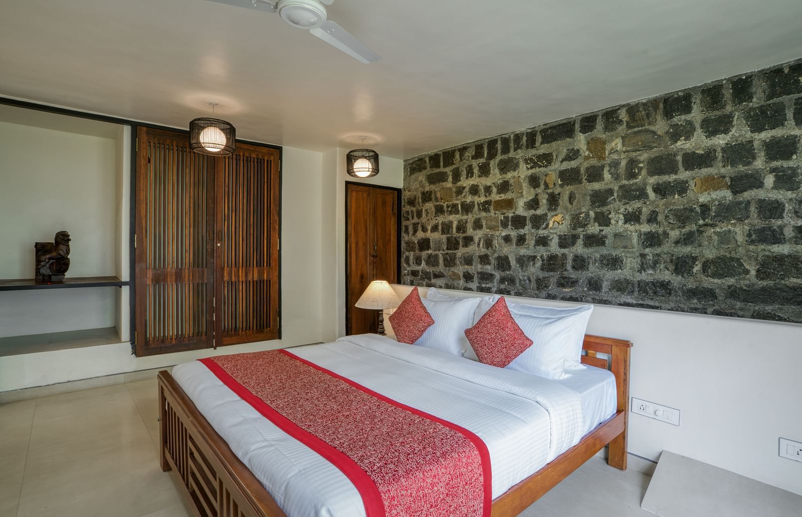 A spacious bedroom with a comfortable bed, red accents, a stone feature wall, and a well-lit, inviting atmosphere. | Mango Hill, Yercaud