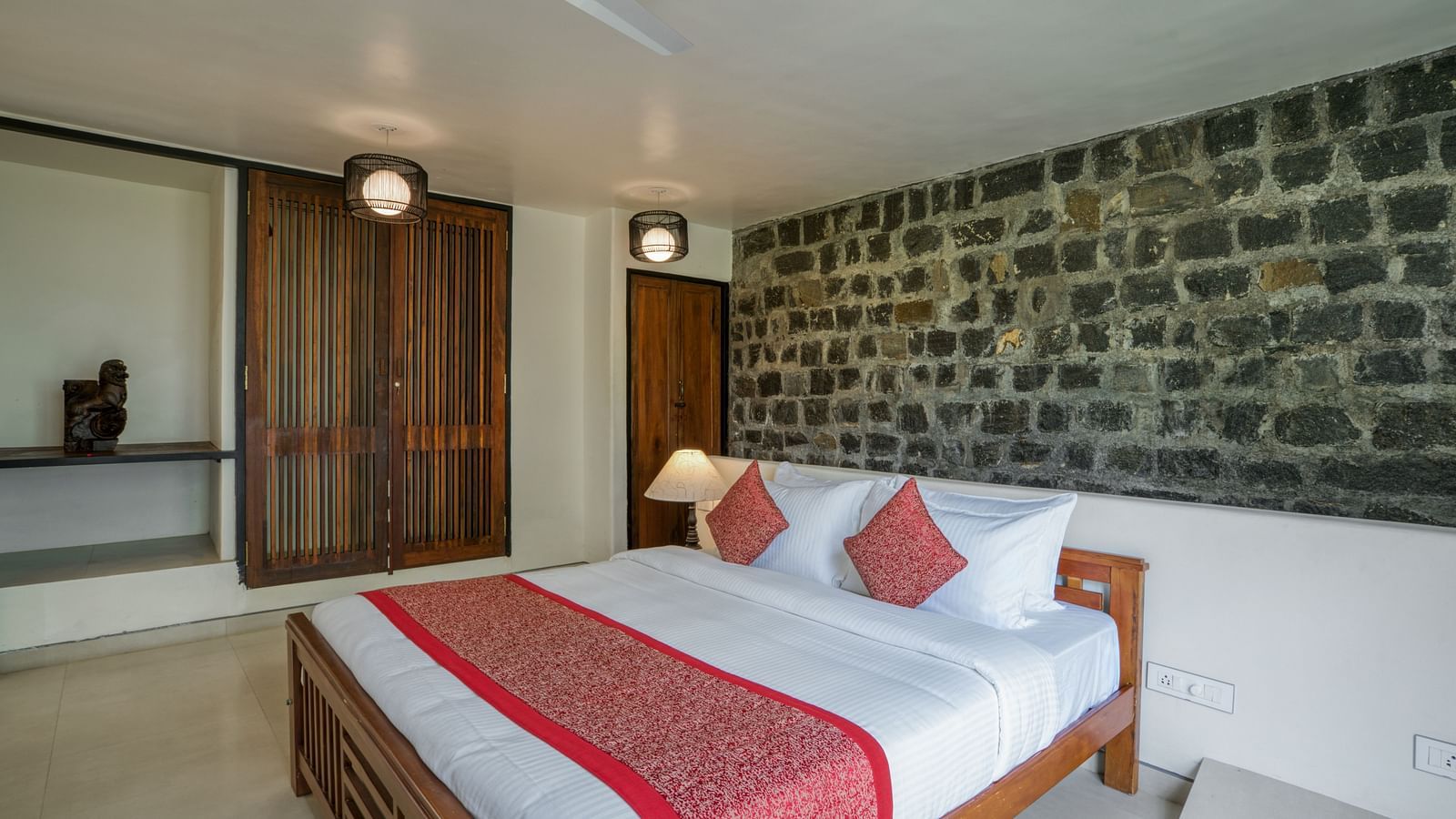 A spacious bedroom with a comfortable bed, red accents, a stone feature wall, and a well-lit, inviting atmosphere. | Mango Hill, Yercaud