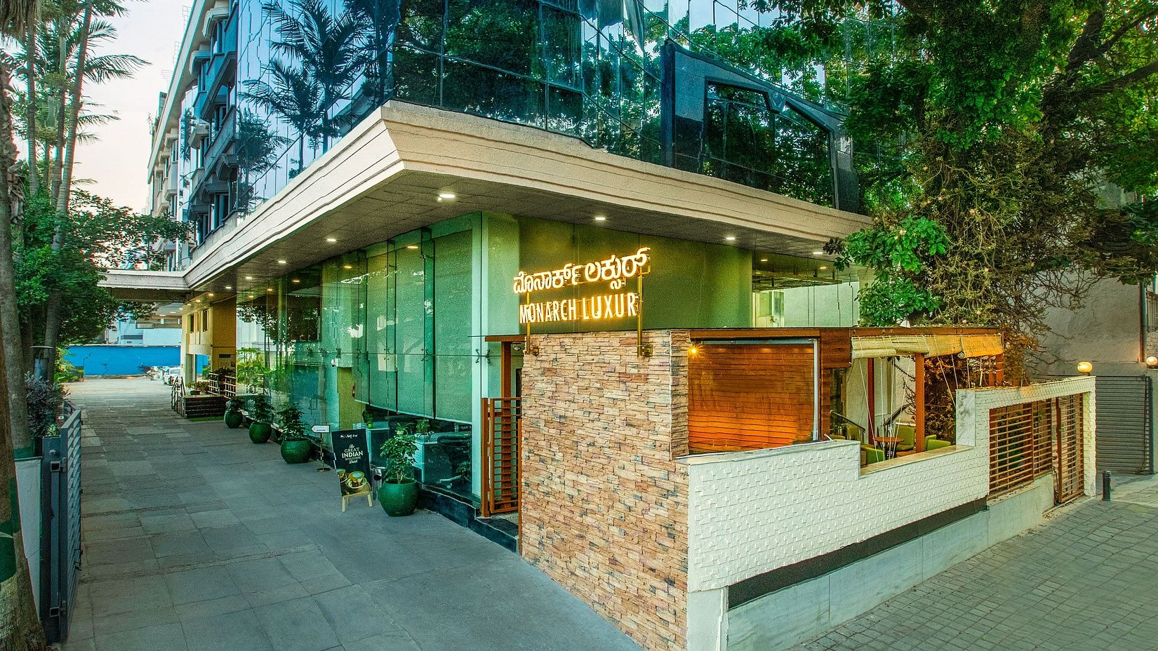 Exterior view of Monarch Luxur Hotel featuring a glass facade, greenery, and a well-maintained entrance.