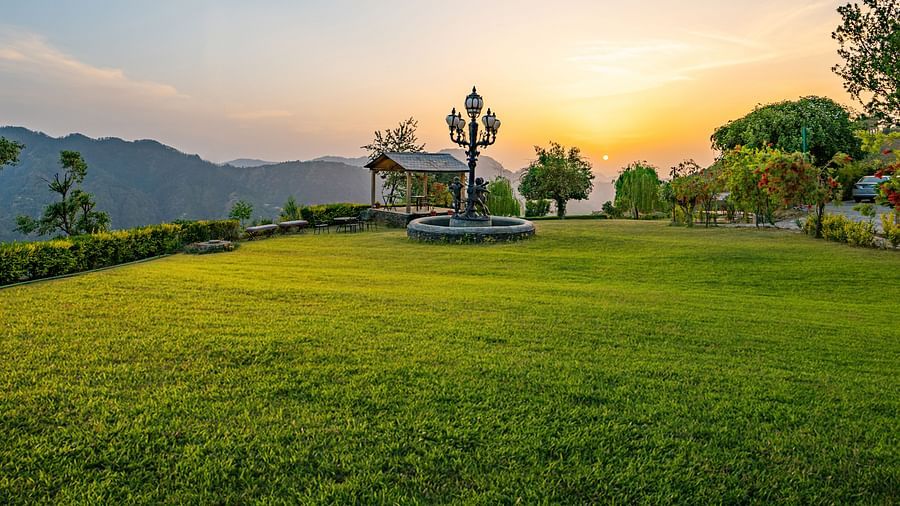 Breathtaking sunset views at The Manor Wellness & Sports Hotel - expansive manicured lawns with ornate lamp post & mountain backdrop creating serene escape.