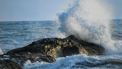 Sea waves crashing on a rock on a sunny day.