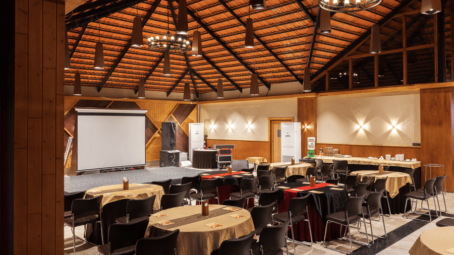 A large banquet hall with a high vaulted wooden ceiling, round dining tables, and a projection screen at Hotel Sonar Bangla, Sundarban.