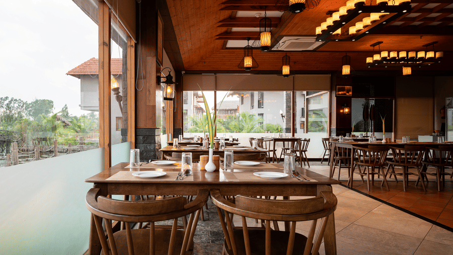 Indoor restaurant area with wooden tables, chairs, and large glass windows at Hotel Sonar Bangla, Sundarban.
