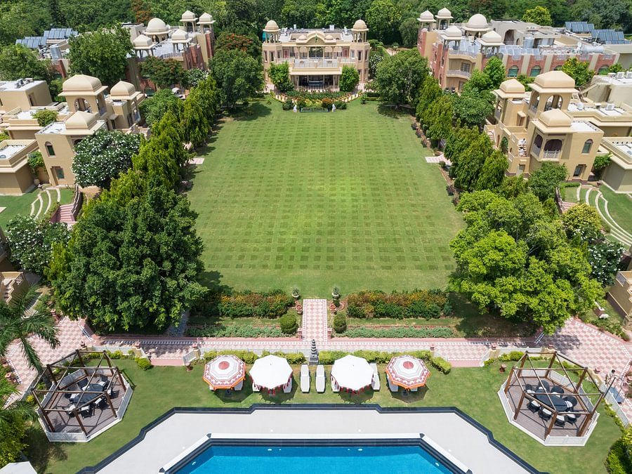 Aerial view of a sprawling resort with a large green lawn, swimming pool, and traditional architecture - Heritage Village Resorts & Spa.