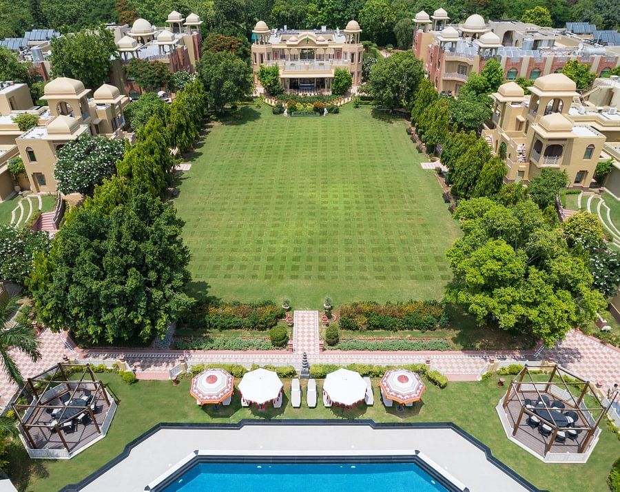 Aerial view of a sprawling resort with a large green lawn, swimming pool, and traditional architecture - Heritage Village Resorts & Spa.