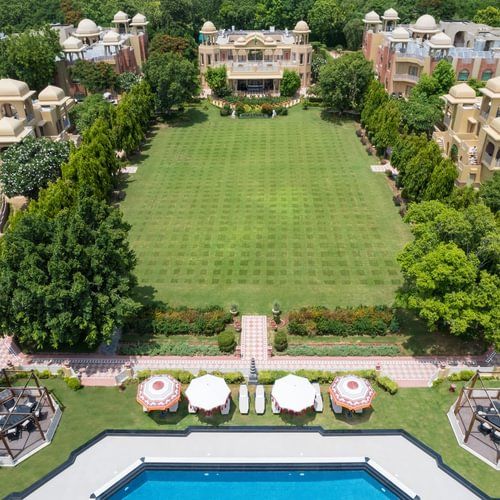 Aerial view of a sprawling resort with a large green lawn, swimming pool, and traditional architecture - Heritage Village Resorts & Spa.