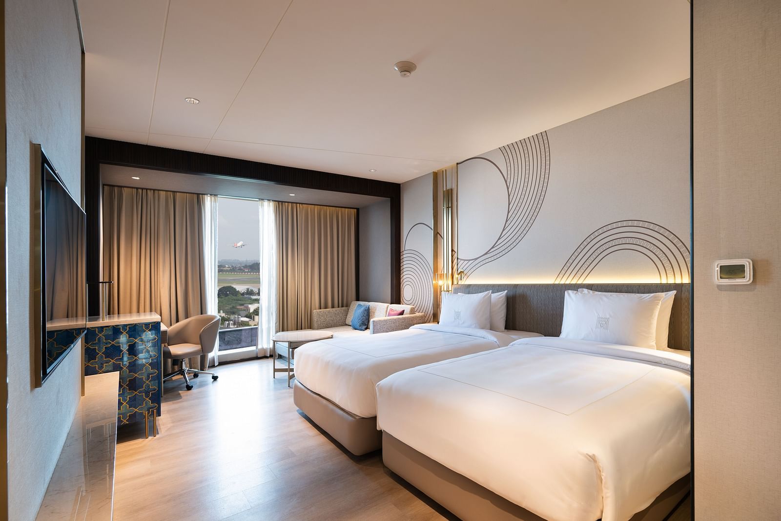 A spacious hotel room with two large beds, a window offering a view, and contemporary design elements at Merlis Hotel, Coimbatore.