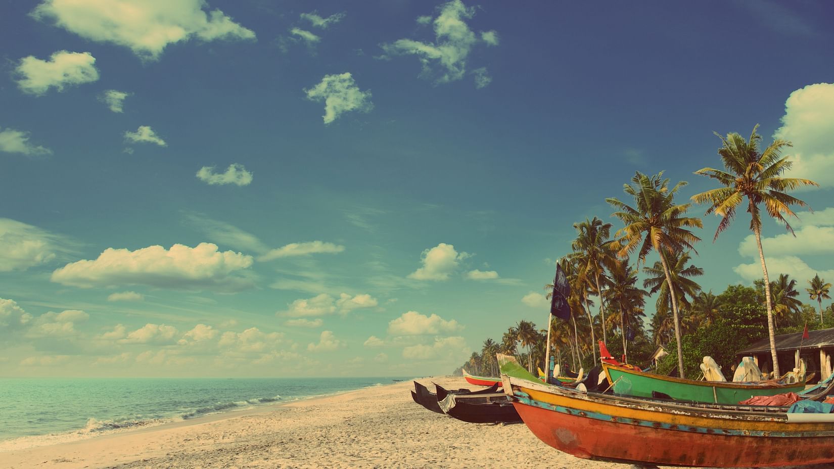 a brown sandy beach with boats kept on the beach and blue sky in the background