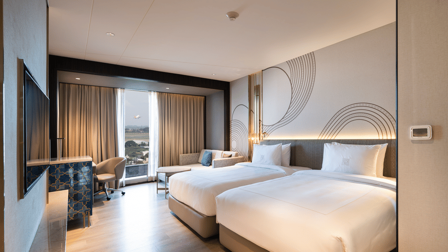 A spacious hotel room with 2 large beds, a window offering a view, and contemporary design elements at Merlis Hotel, Coimbatore.